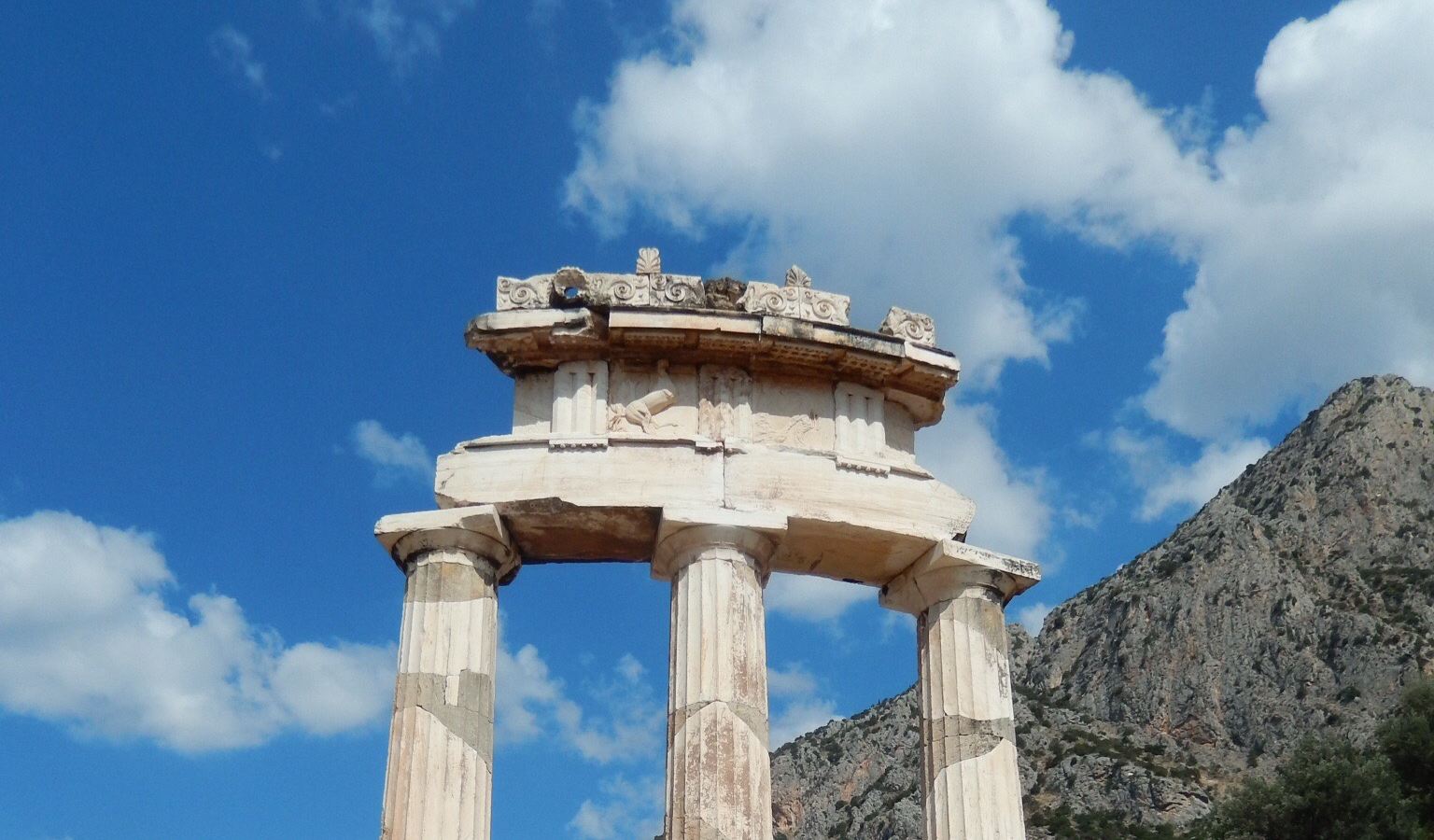 De Tholos van Delphi: een ronde zuilentempel tegen een blauwe lucht, het beeld uit het logo van het kantoor